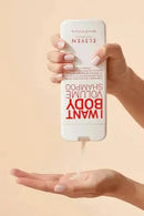 Hand holding a bottle of 'I Want Body Volume' shampoo with product being dispensed onto another hand against a beige background - Hair Care Canada